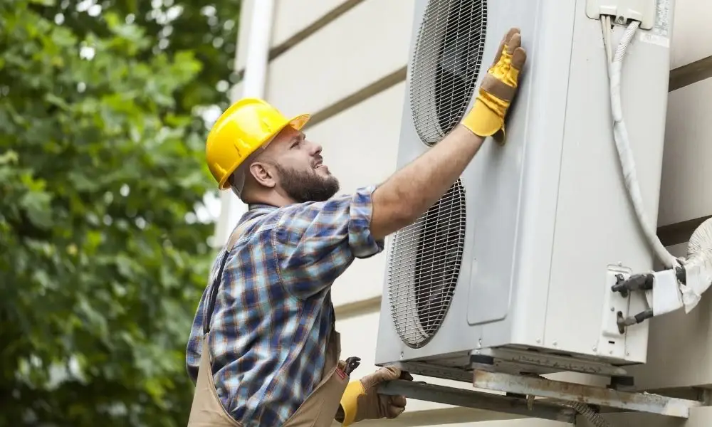 HVAC technician inspecting and servicing an outdoor air conditioning condenser unit during residential maintenance.
