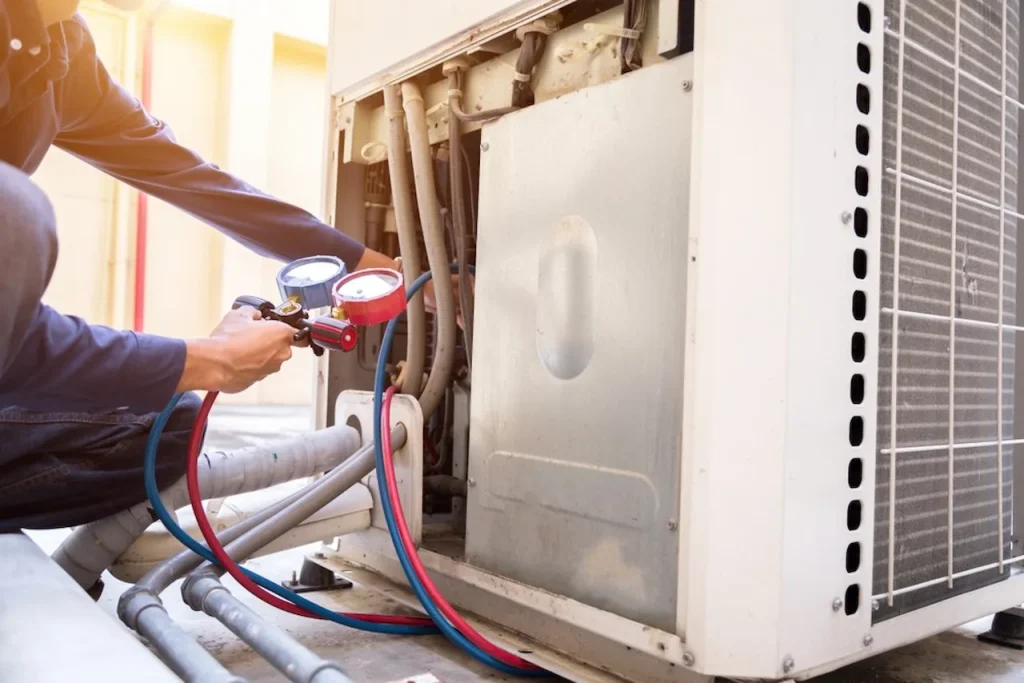 HVAC technician inspecting and servicing an outdoor air conditioning unit using pressure gauges during routine maintenance and system diagnostics.