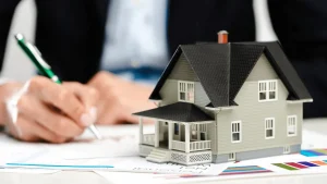 House model on architectural plans with a person reviewing real estate documents.